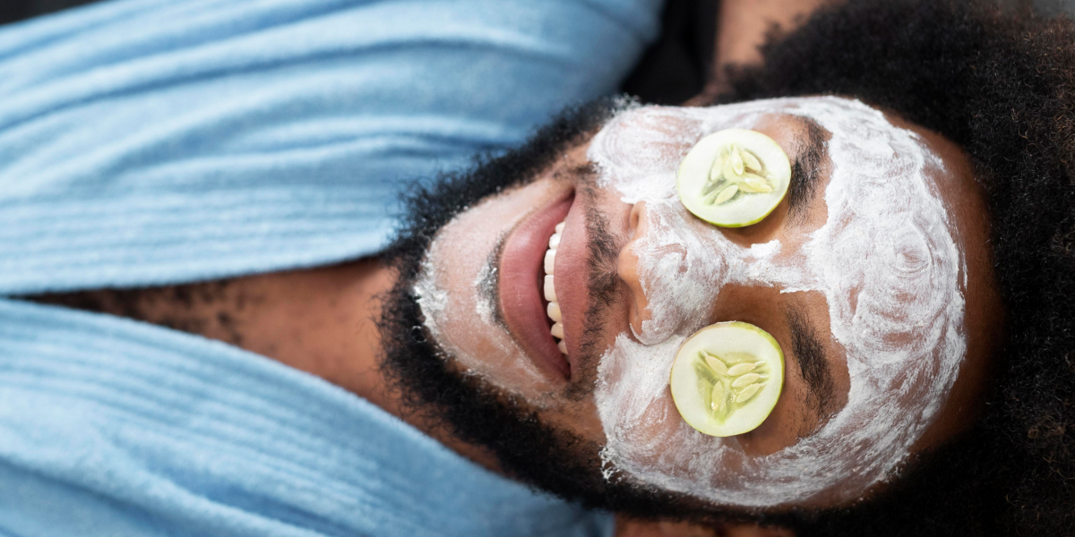 A man of color with a facial mask and cucumber